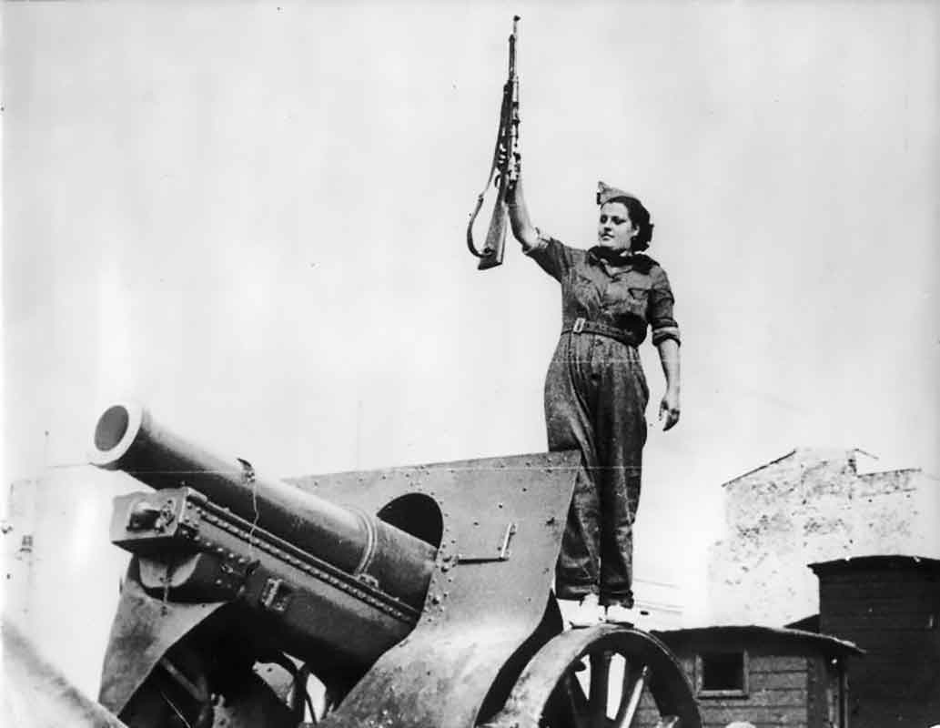 Donna della milizia posa con un fucile sopra un cannone